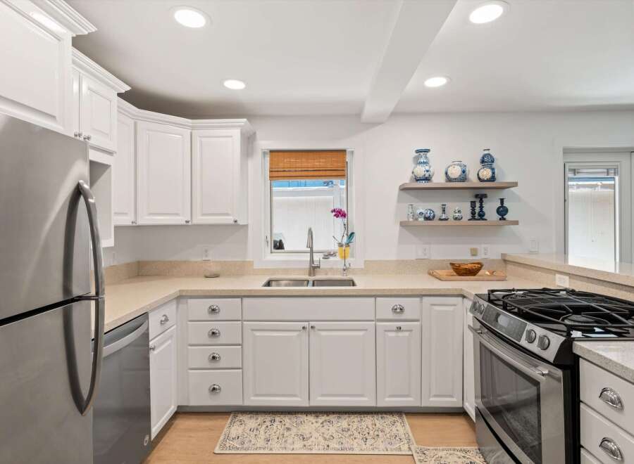 This modern kitchen features sleek white cabinetry and stainless steel appliances, including a refrigerator and a gas range.