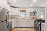 This modern kitchen features sleek white cabinetry and stainless steel appliances, including a refrigerator and a gas range.