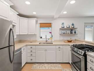 This modern kitchen features sleek white cabinetry and stainless steel appliances, including a refrigerator and a gas range.
