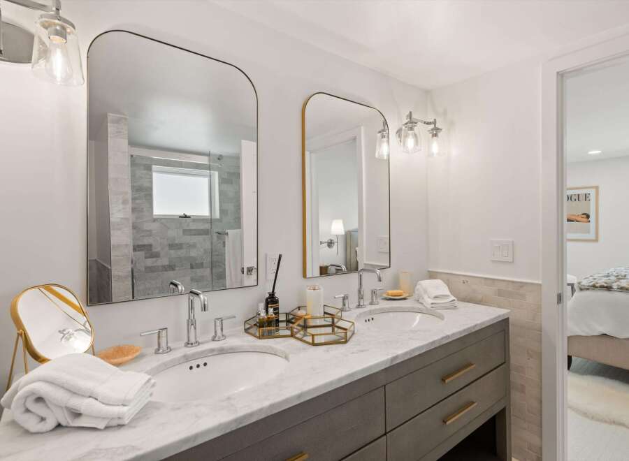 This modern bathroom features a spacious double vanity with marble countertops and sleek gray cabinetry.