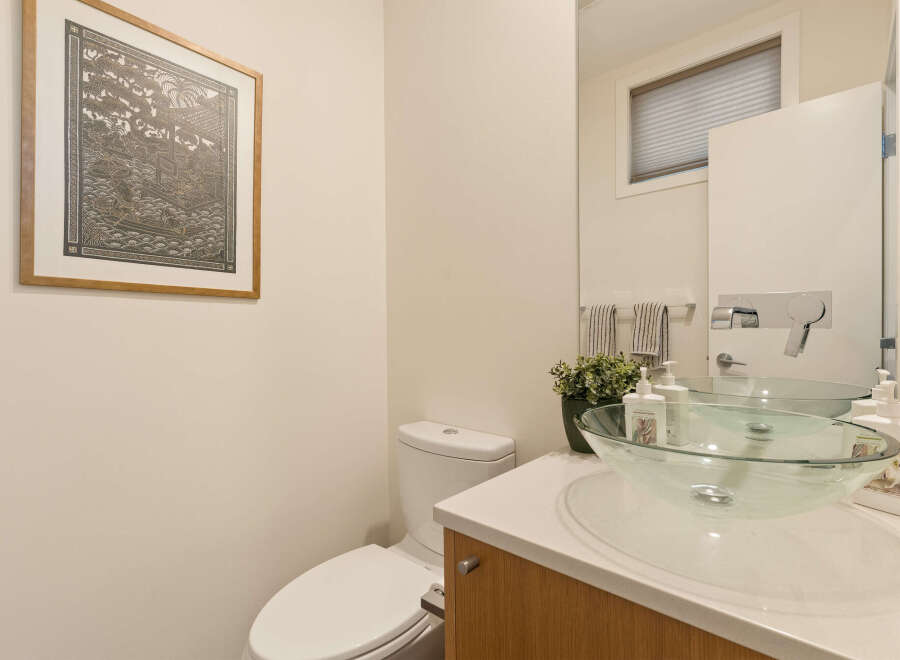 This modern bathroom features a sleek white toilet and a stylish glass vessel sink atop a light wood vanity.
