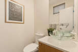 This modern bathroom features a sleek white toilet and a stylish glass vessel sink atop a light wood vanity.