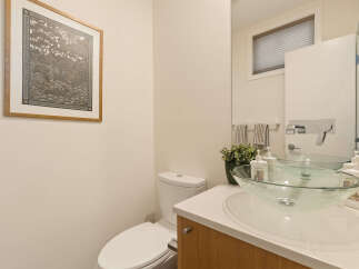 This modern bathroom features a sleek white toilet and a stylish glass vessel sink atop a light wood vanity.
