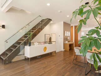 Experience modern living in this stunning home featuring a sleek staircase with glass railings and a minimalist white credenza.