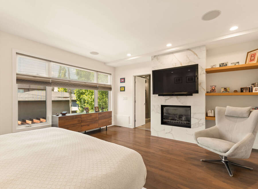 Experience luxury living in this master suite featuring a modern gas fireplace with marble surround and a wall-mounted television.