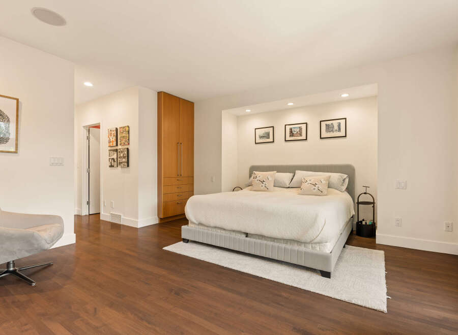 This spacious bedroom features a comfortable king-sized bed with plush pillows, set against a backdrop of recessed lighting and framed artwork.