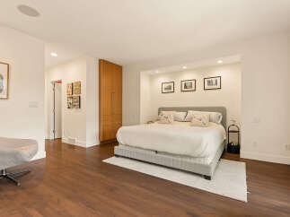 This spacious bedroom features a comfortable king-sized bed with plush pillows, set against a backdrop of recessed lighting and framed artwork.