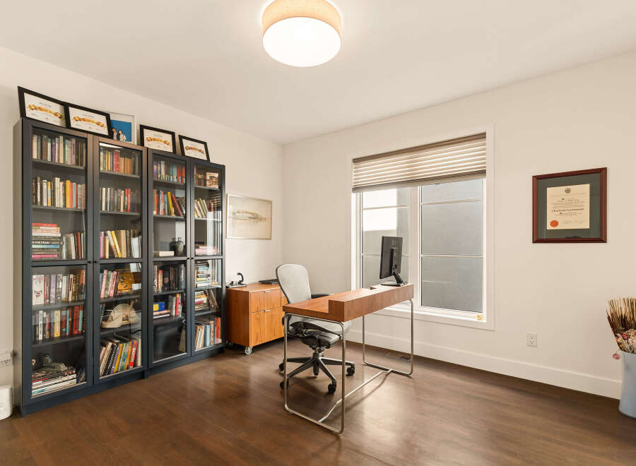 This home office features a large window with blinds, a modern wooden desk with a computer, and a comfortable office chair.