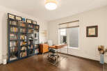This home office features a large window with blinds, a modern wooden desk with a computer, and a comfortable office chair.
