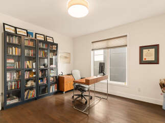 This home office features a large window with blinds, a modern wooden desk with a computer, and a comfortable office chair.