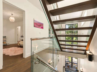 Experience modern luxury with this stunning staircase featuring floating wooden treads and sleek glass railings.