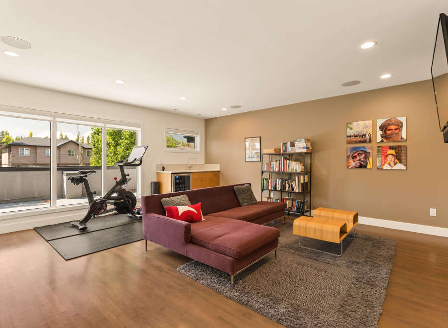 This modern living space seamlessly blends a home gym with a comfortable lounge area, featuring a Peloton bike and a plush sectional sofa.