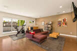 This modern living space seamlessly blends a home gym with a comfortable lounge area, featuring a Peloton bike and a plush sectional sofa.