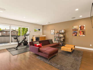 This modern living space seamlessly blends a home gym with a comfortable lounge area, featuring a Peloton bike and a plush sectional sofa.
