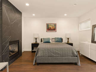 Experience modern luxury in this stunning bedroom featuring a sleek, dark marble fireplace as a striking focal point.