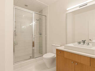 This modern bathroom features a sleek glass-enclosed shower with white tiled walls, a minimalist toilet, and a floating vanity with a rectangular vessel sink.