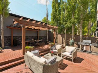 Enjoy outdoor living with this spacious wooden deck, featuring a covered pergola for shade and a dining area.