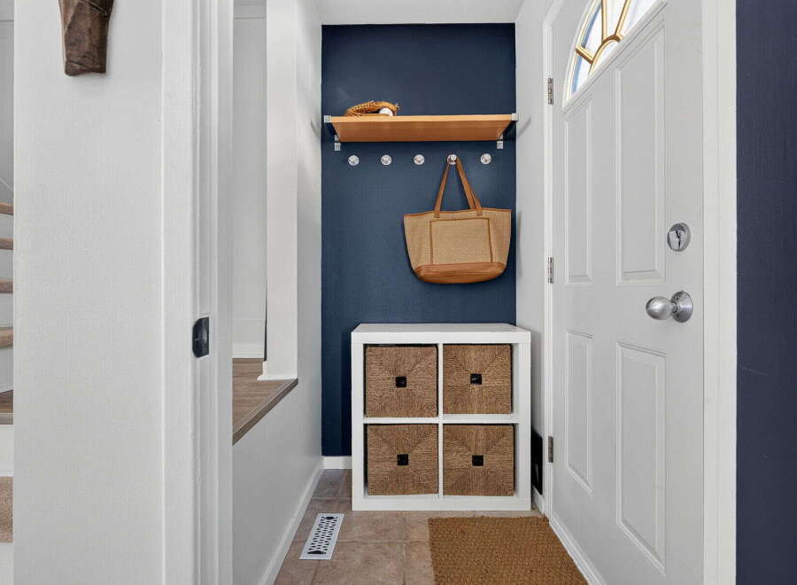 Welcome guests into a charming entryway featuring a navy accent wall, a floating wood shelf with decorative items, and a convenient storage cube with woven baskets.
