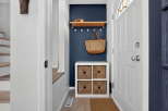 Welcome guests into a charming entryway featuring a navy accent wall, a floating wood shelf with decorative items, and a convenient storage cube with woven baskets.