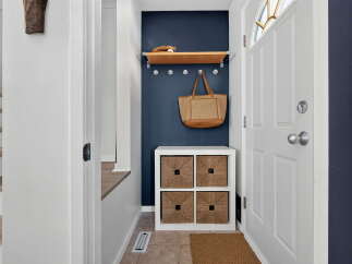 Welcome guests into a charming entryway featuring a navy accent wall, a floating wood shelf with decorative items, and a convenient storage cube with woven baskets.
