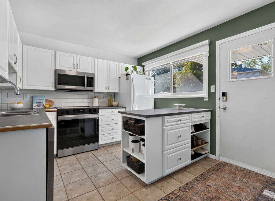 Discover this charming kitchen featuring white cabinetry, a stainless steel microwave, and a sleek oven.