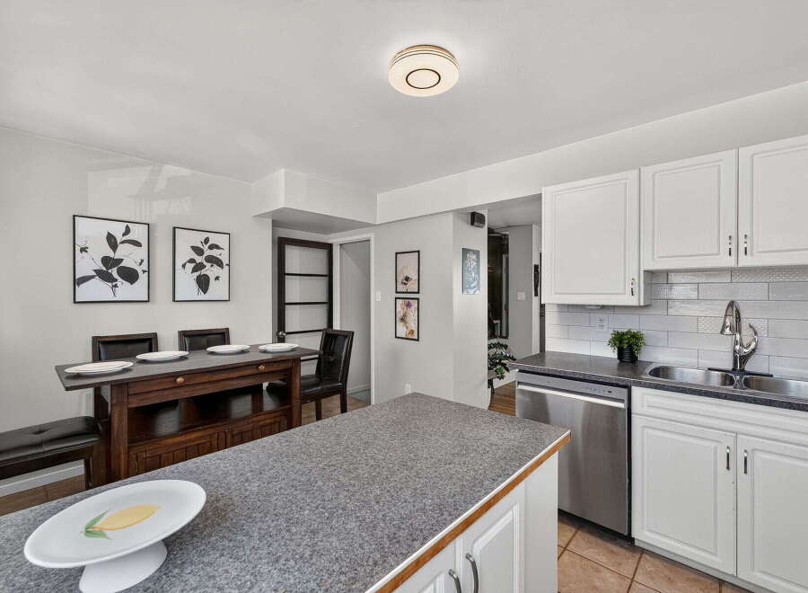 This spacious kitchen features white cabinetry, a sleek stainless steel dishwasher, and a double sink with a modern faucet.