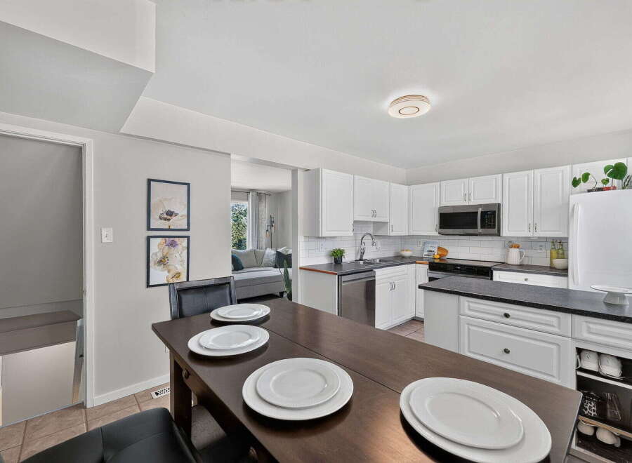 This spacious kitchen features white cabinetry, a sleek black countertop, and a convenient breakfast bar area perfect for casual dining.