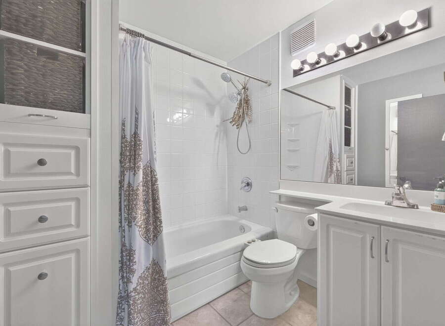 This bright and clean bathroom features a white tiled shower-tub combination with a patterned shower curtain.