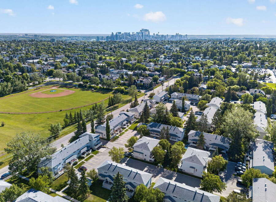 Discover this charming residential neighborhood featuring a baseball field and a distant city skyline.