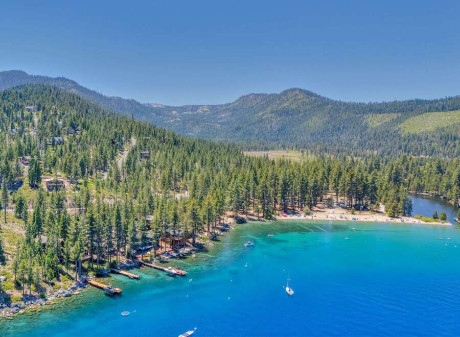 Experience luxury living with this stunning aerial view of a lakeside property nestled amidst a dense pine forest.