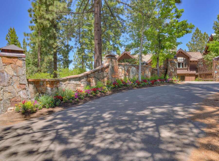 Discover this stunning property featuring a grand stone entrance with a curved wall adorned with vibrant flowers, leading to a beautiful wooden home.