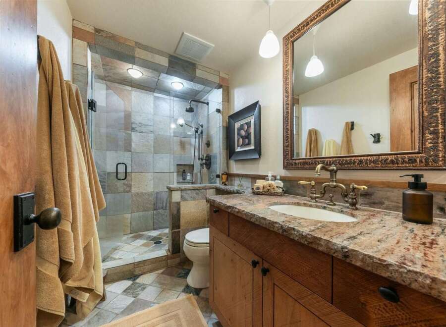 Experience rustic elegance in this beautifully appointed bathroom, featuring a spacious walk-in shower with intricate tile work and dual shower heads.