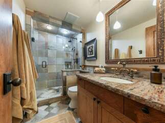 Experience rustic elegance in this beautifully appointed bathroom, featuring a spacious walk-in shower with intricate tile work and dual shower heads.