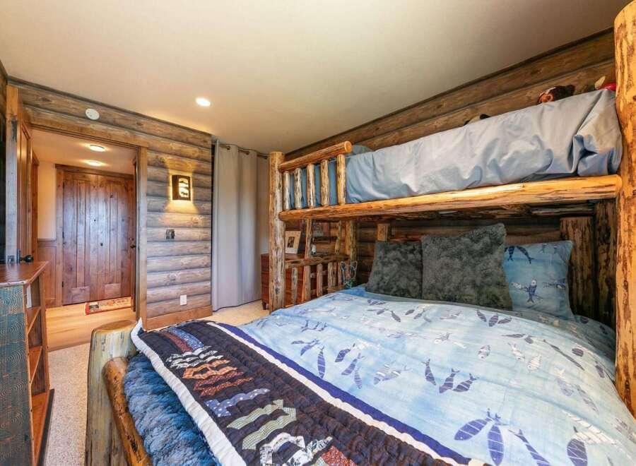 Experience rustic charm in this unique bedroom featuring a log bunk bed and cozy wood-paneled walls.