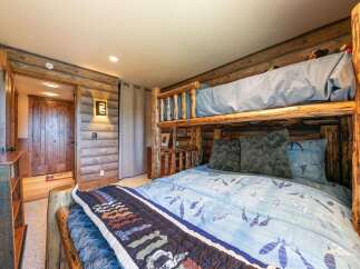 Experience rustic charm in this unique bedroom featuring a log bunk bed and cozy wood-paneled walls.