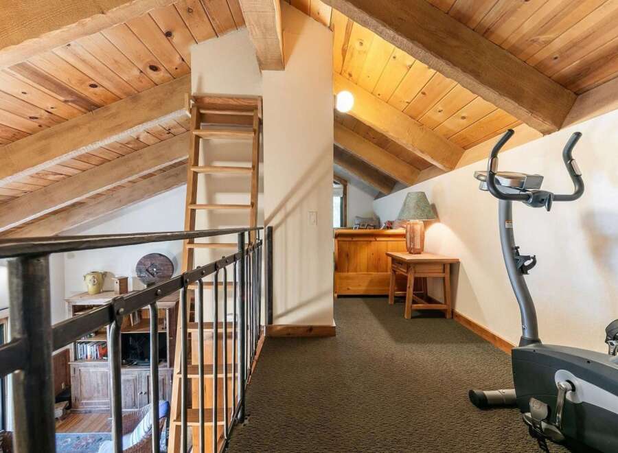 Ascend to this charming loft space, featuring exposed wooden beams and a rustic ladder leading to an upper level.