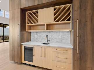 Experience luxury living with this stunning wet bar, featuring a built-in wine rack, sleek marble countertops, and a modern undermount sink.