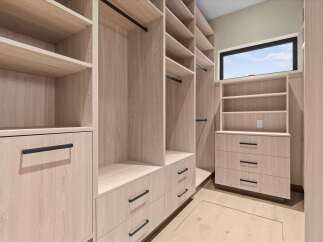 Step into this spacious walk-in closet, featuring custom light wood cabinetry and ample storage solutions.