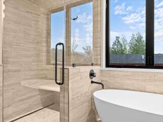 Experience luxury in this modern bathroom featuring a spacious glass-enclosed shower with a built-in bench and elegant stone tilework.