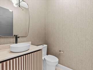 This modern powder room features a sleek vanity with a vessel sink and a matte black faucet, complemented by a rounded mirror and textured wallpaper.