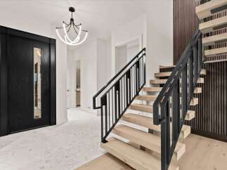 Step into modern luxury with this stunning entryway featuring a sleek black pivot door and a captivating multi-tiered chandelier.