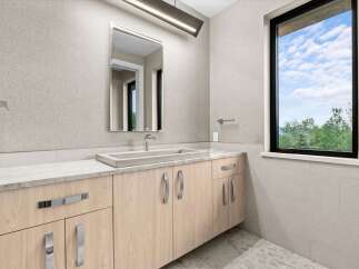 This modern bathroom features a sleek concrete sink atop a light wood vanity with chrome hardware.