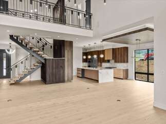 Experience modern luxury in this stunning open-concept living space, featuring a sleek floating staircase and a gourmet kitchen with rich wood cabinetry and a marble-topped island.