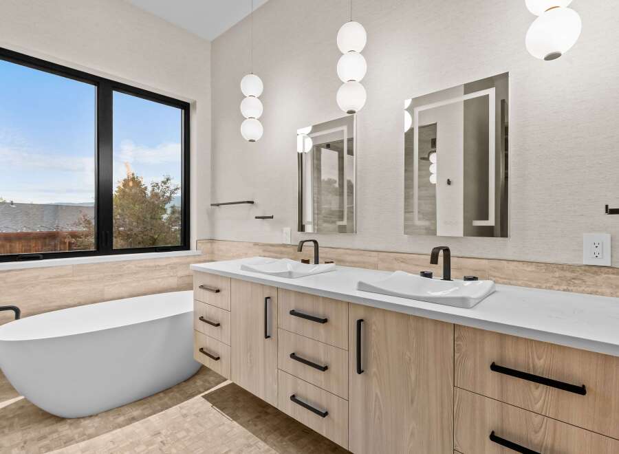 Experience luxury in this modern bathroom featuring a freestanding soaking tub and a dual vanity with sleek wood cabinetry and integrated sinks.