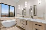 Experience luxury in this modern bathroom featuring a freestanding soaking tub and a dual vanity with sleek wood cabinetry and integrated sinks.