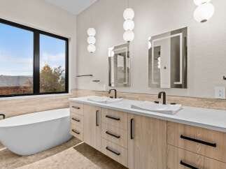Experience luxury in this modern bathroom featuring a freestanding soaking tub and a dual vanity with sleek wood cabinetry and integrated sinks.