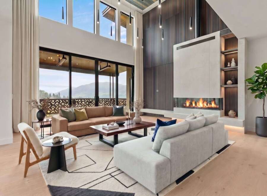 Experience luxurious living in this stunning modern living room, featuring a grand fireplace and expansive windows with breathtaking mountain views.