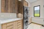 This modern laundry room boasts a stacked washer and dryer unit, complemented by sleek wood cabinetry and elegant marble countertops.