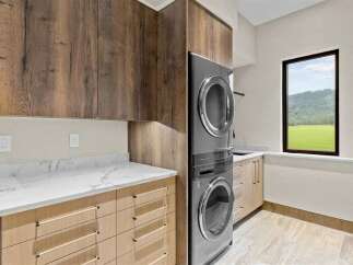 This modern laundry room boasts a stacked washer and dryer unit, complemented by sleek wood cabinetry and elegant marble countertops.