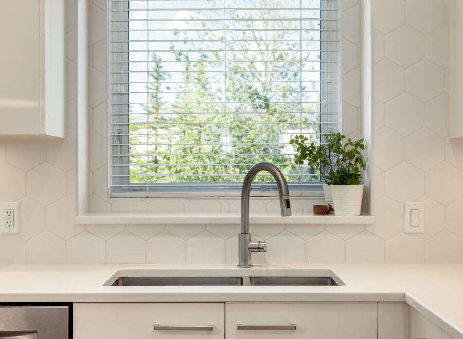 This modern kitchen features a sleek stainless steel faucet over a double basin sink, complemented by a hexagonal tile backsplash.